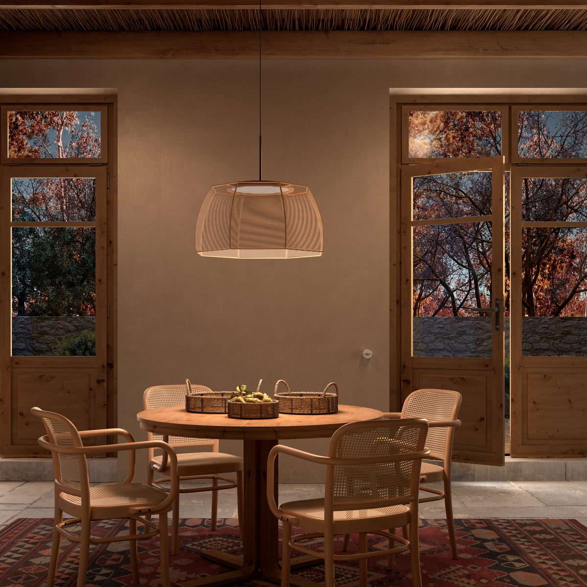 Tanit S/61 fabric LED pendant light with a wide faceted beige cotton shade on a matt black stem, hung above a round wooden dining table with rattan chairs.