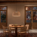 Tanit S/61 fabric LED pendant light with a wide faceted beige cotton shade on a matt black stem, hung above a round wooden dining table with rattan chairs.