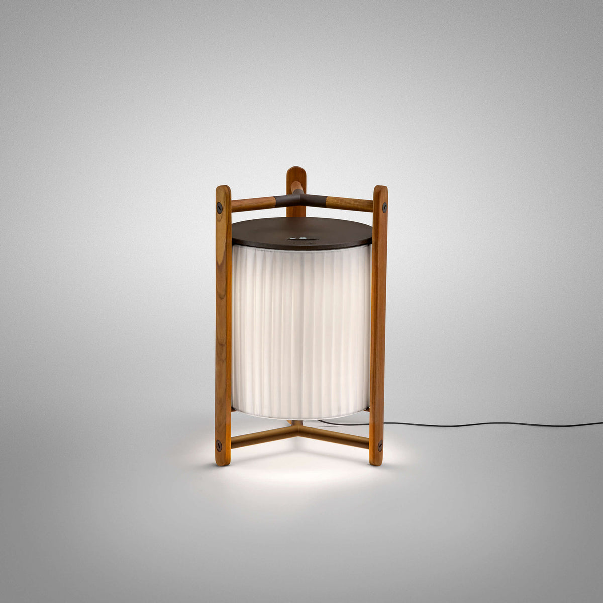 Kando M/40 lantern-style LED table lamp with pleated white translucent ribbon shade in a brown wooden three-legged frame, dark top disc, on a plain light grey background.