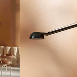Opuntia 180 Aluminium LED Wall Light with a slim extending arm and dome-shaped black head, shown mounted on a peach wall in a living room setting.