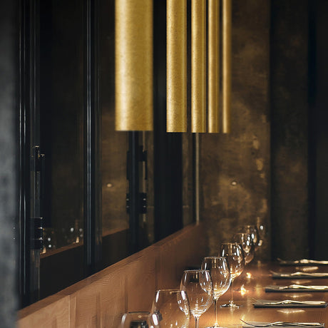 To-Be Aluminium Linear LED Pendant Light in Gold Leaf, slim tubular fixtures grouped above a wooden dining counter with wine glasses.