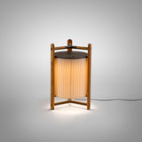 Kando M/40 Ribbon LED table lamp with cream pleated fabric shade and teak wood tripod frame, lit against a plain light grey background.