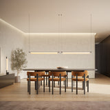Two Ombra Fabric LED pendant lights, slim cylindrical off-white diffusers on thin wires, hung in black above a dining table with leather chairs.