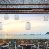 Nans S/16 Outrack woven LED outdoor track pendants in beige shades on a track system, suspended over a coastal terrace dining area at sunset with sea views.