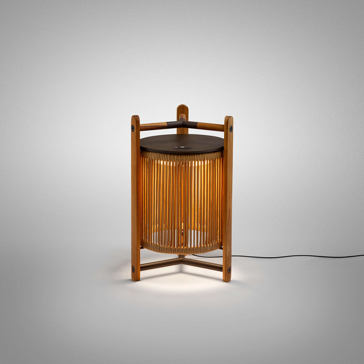 Kando M/40 Wood LED table lamp with a cylindrical sand-coloured strand shade inside a three-post teak frame, dark brown top disc, integrated LED, shown on a plain light grey background.