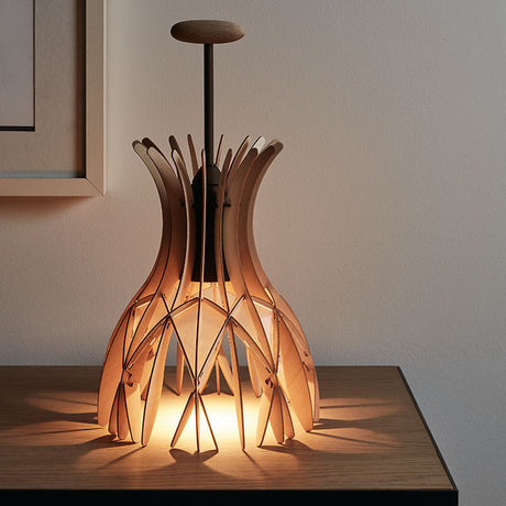 Domita M/36 wood bell table lamp with interlocking natural beech slats forming a bell-shaped shade, brown central stem and flat round knob, lit on a wooden table against a plain wall.