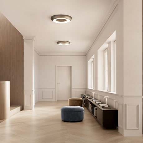 Superbold LED flush ceiling lights in brushed bronze with glowing white halo rings, shown mounted in a hallway above wood-panelled shelving and parquet flooring.