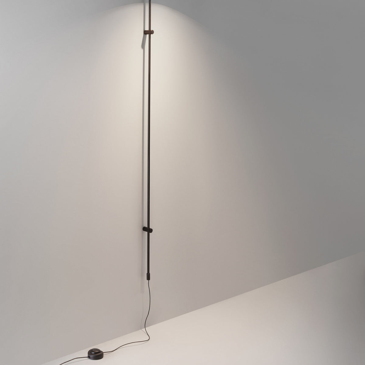 Platet A/05 Aluminium LED Wall Light with slim vertical rod in dark brown, mounted on a neutral wall and extending from floor to ceiling.