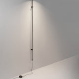 Platet A/05 Aluminium LED Wall Light with slim vertical rod in dark brown, mounted on a neutral wall and extending from floor to ceiling.