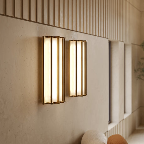 Roma Glass LED Wall Light in Brushed Bronze, two half-round fittings with vertical bars and warm white diffusers glowing on a textured wall, shown in a living room setting.