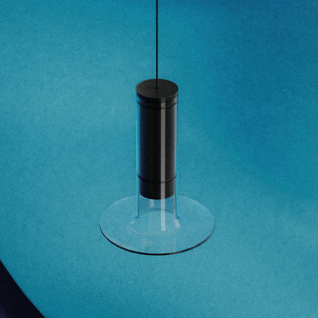 Auriel Glass Candle LED Pendant Light in matt black, a slim cylinder inside a clear glass tube with a flat glass disc base, suspended on a fine cable against a blue background.