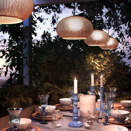 Garota Hang globe pendant lights in woven ivory white finish, shown in varied sizes over an outdoor dining table set with candles and glassware amid evening garden foliage.