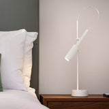 Tubino Aluminium LED Table Lamp in white, with a slim upright stem, angled cylindrical head and arched cable, shown lit on a wooden bedside table.
