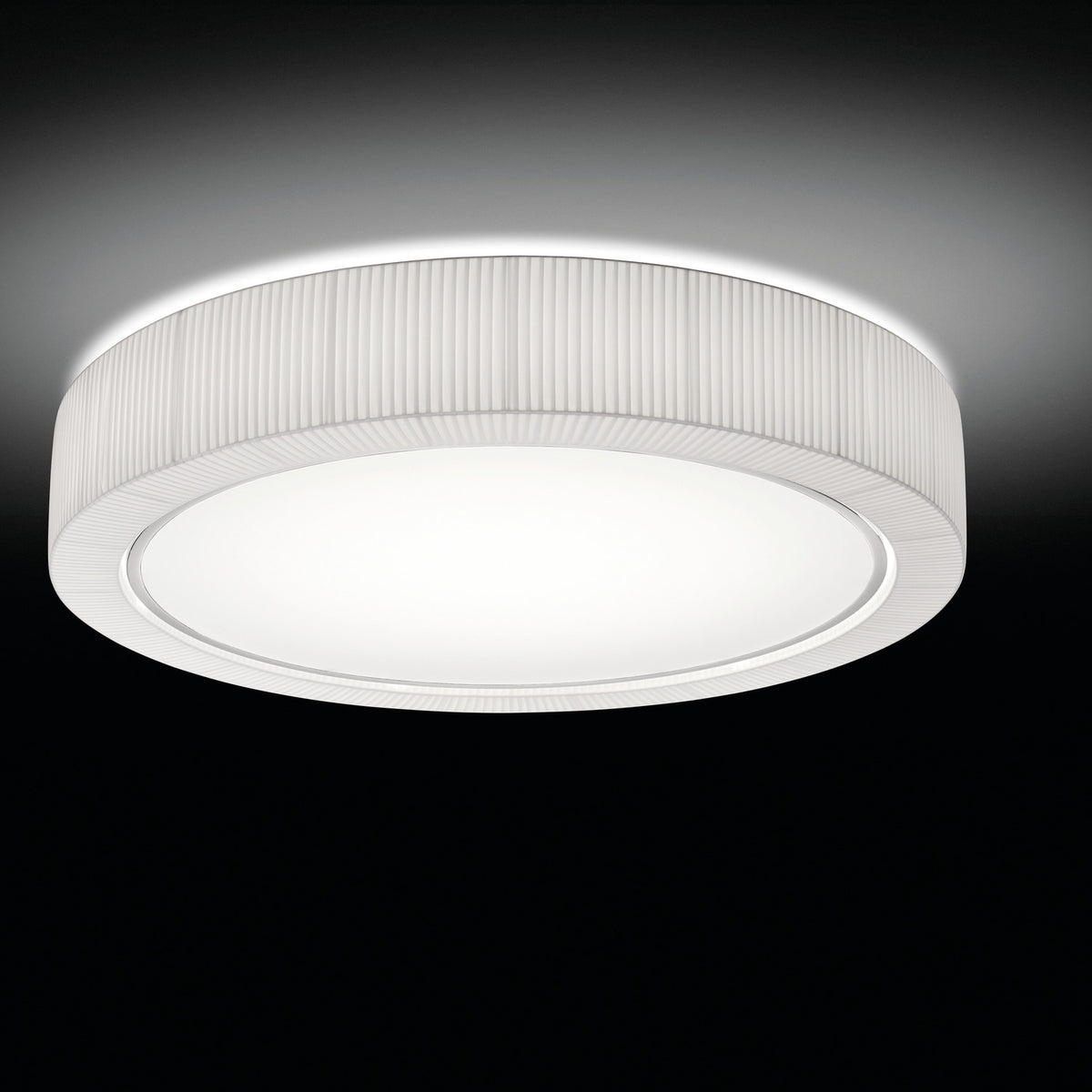 Urban PF/90 Ribbon LED ceiling light with a round drum shade in pleated white translucent fabric over an iron frame, broad white diffuser with silver trim, shown glowing against a dark background.