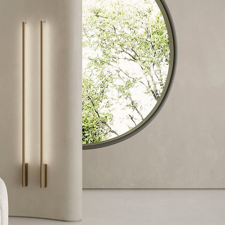Hilow Line linear wall lights in brushed bronze, two slim 150cm rods mounted on a curved beige wall beside a round window overlooking greenery.