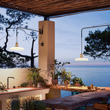 Marietta 32 A/98 outdoor wall lights with long slim arms and pleated white cone shades, mounted on a pergola post and beam above an outdoor kitchen and dining area overlooking the sea.