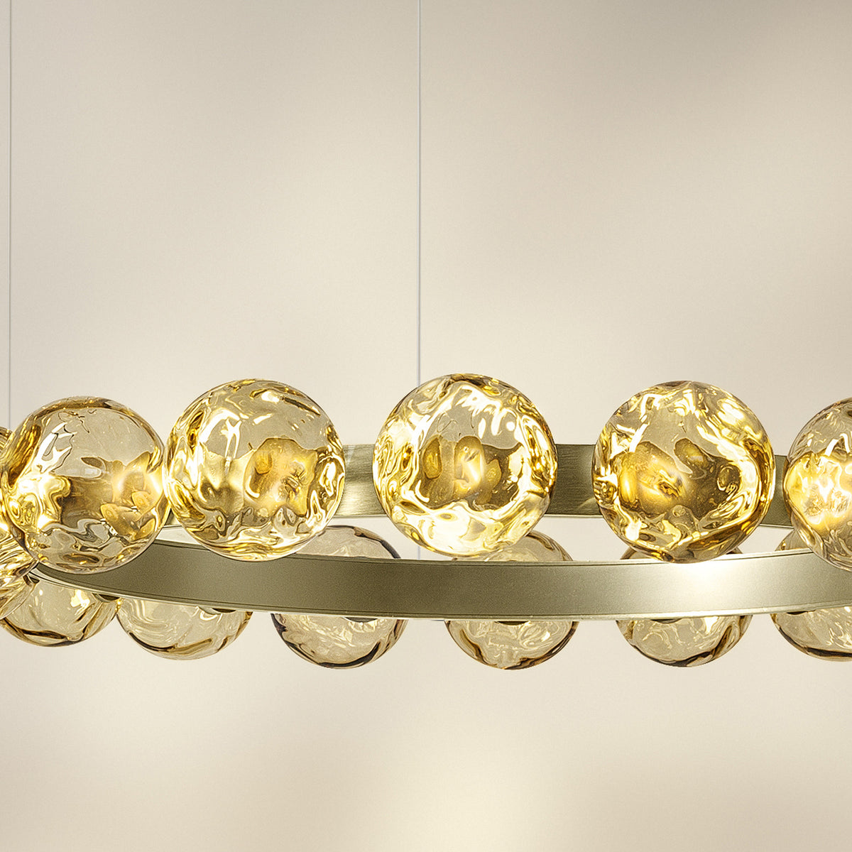 Murané R 25 ring chandelier, close-up of brushed champagne band with caramel glass spheres lit from within, set against a plain light background.