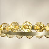 Close-up of the Murané R 18 ring chandelier, a brushed champagne band lined with rippled amber glass spheres glowing with integrated warm-white LED light.