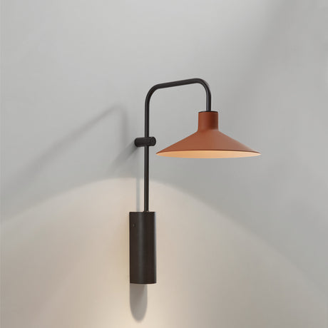 Platet A/02 wall light in black aluminium with a terracotta cone shade on a hooked arm and cylindrical wall-mounted body, shown against a plain light grey background.