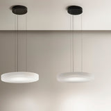 Two Côte pendant lights with shallow frosted white glass discs and ribbed undersides, hung on black ceiling mounts against a neutral wall.