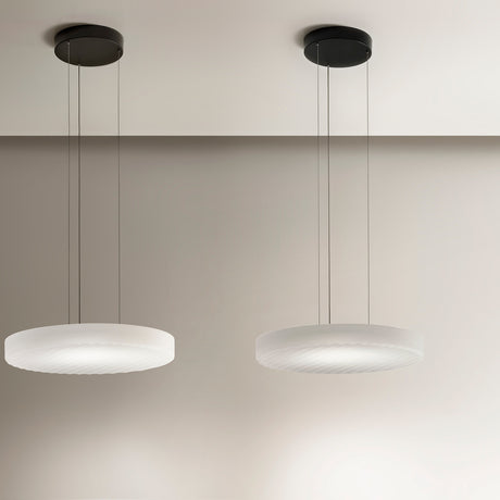 Two Côte pendant lights with shallow frosted white glass discs and ribbed undersides, hung on black ceiling mounts against a neutral wall.