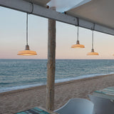 Marietta S/32 Dome LED Outdoor Pendant Light in white, with pleated dome shades on black cables, shown hanging from a beach pavilion beam against a sea and sky backdrop.