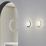 Zero Round Aluminium Ring LED Wall Light in black and brass finishes, shown illuminated on a grey wall beside a matching pendant version in an arched interior.