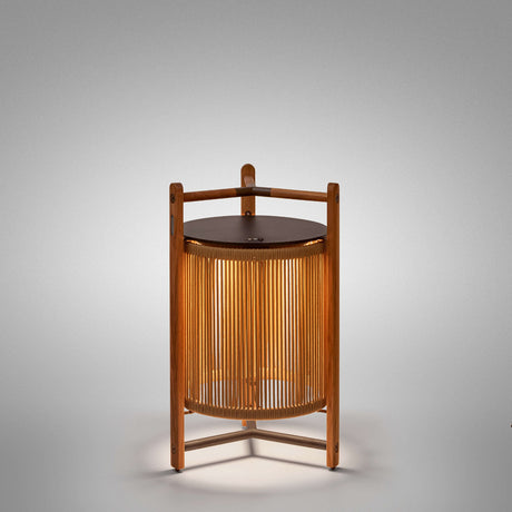 Kando P/76/R rechargeable outdoor floor lamp, lantern-shaped with sand nautical cord cylinder, teak wood frame, dark brown top disc and tripod feet, lit, on a plain light grey background.
