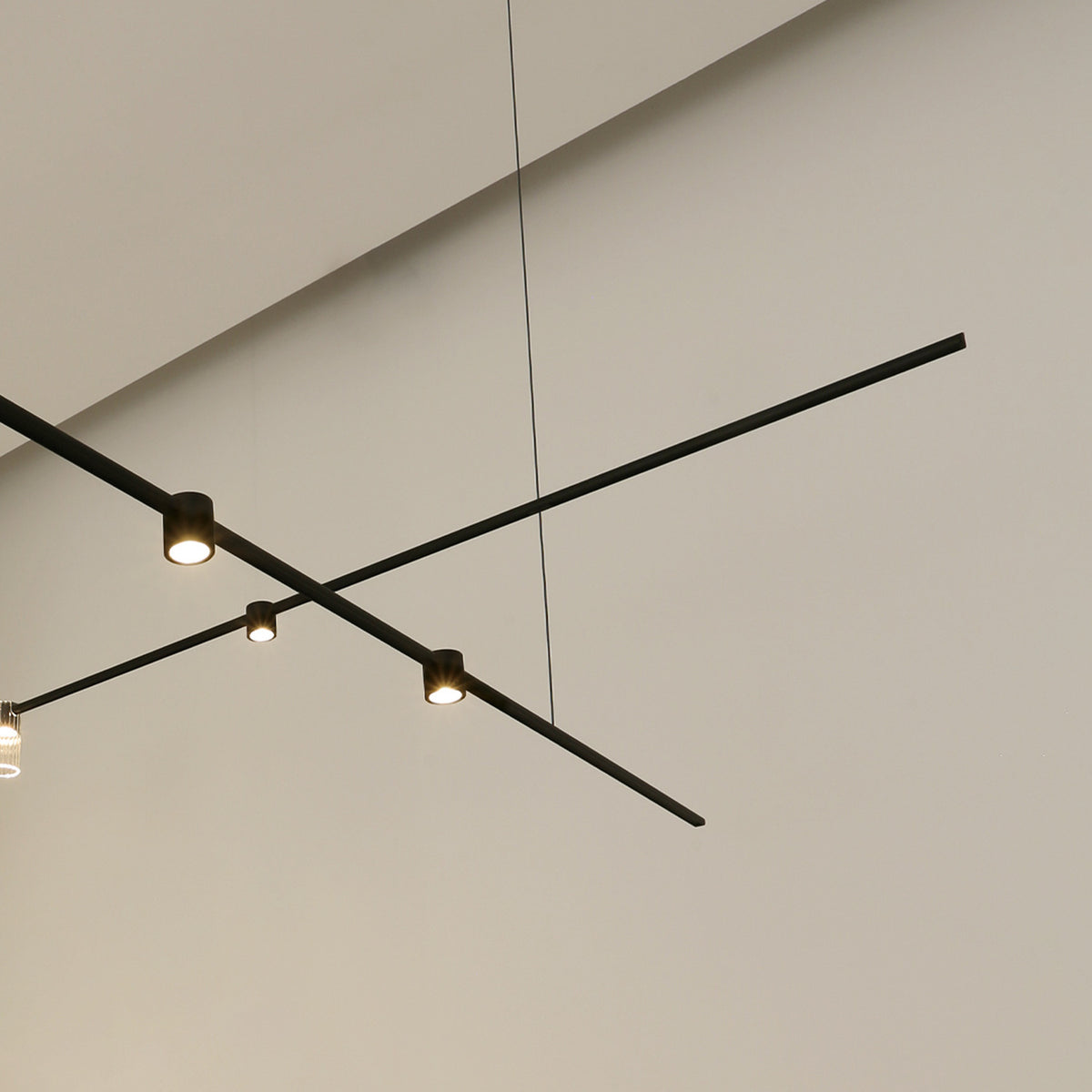 SIS Spotlight 36° cylinder LED track spotlights in black, mounted on crossing ceiling tracks, casting warm light against a plain light grey ceiling.