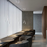 Tubino Aluminium LED Pendant Light in white, slim cylindrical heads on fine cables at varied drop heights, shown grouped above a seating area with grey armchairs and round tables.