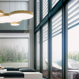 Castle S120 Aluminium LED Pendant Light in brass finish, shown as round drum-shaped fixtures with white diffusers, grouped above a living room seating area with floor-to-ceiling windows.