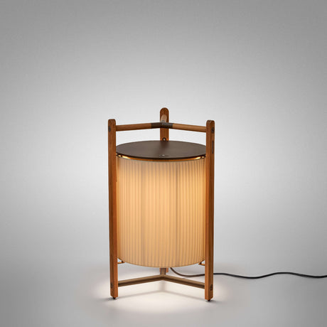 Kando P/76 Ribbon LED floor lamp with a cream pleated cylinder shade in a teak wood tripod frame and round brown top, lit against a plain grey background.