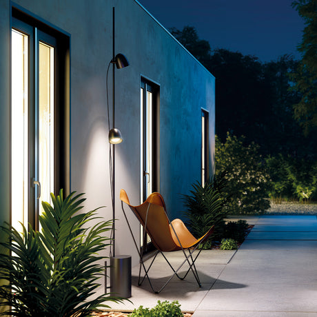 Speers Outdoor Stem 120cm, a slim black IP54-rated floor stem fitted with two angled LED heads, shown lighting a patio seating area beside a house at night.
