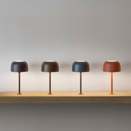 Bol M/33 dome table lamp in textured grey blue, shown third among four colour options with rounded aluminium shade, slim stem and round foot on a wooden shelf.