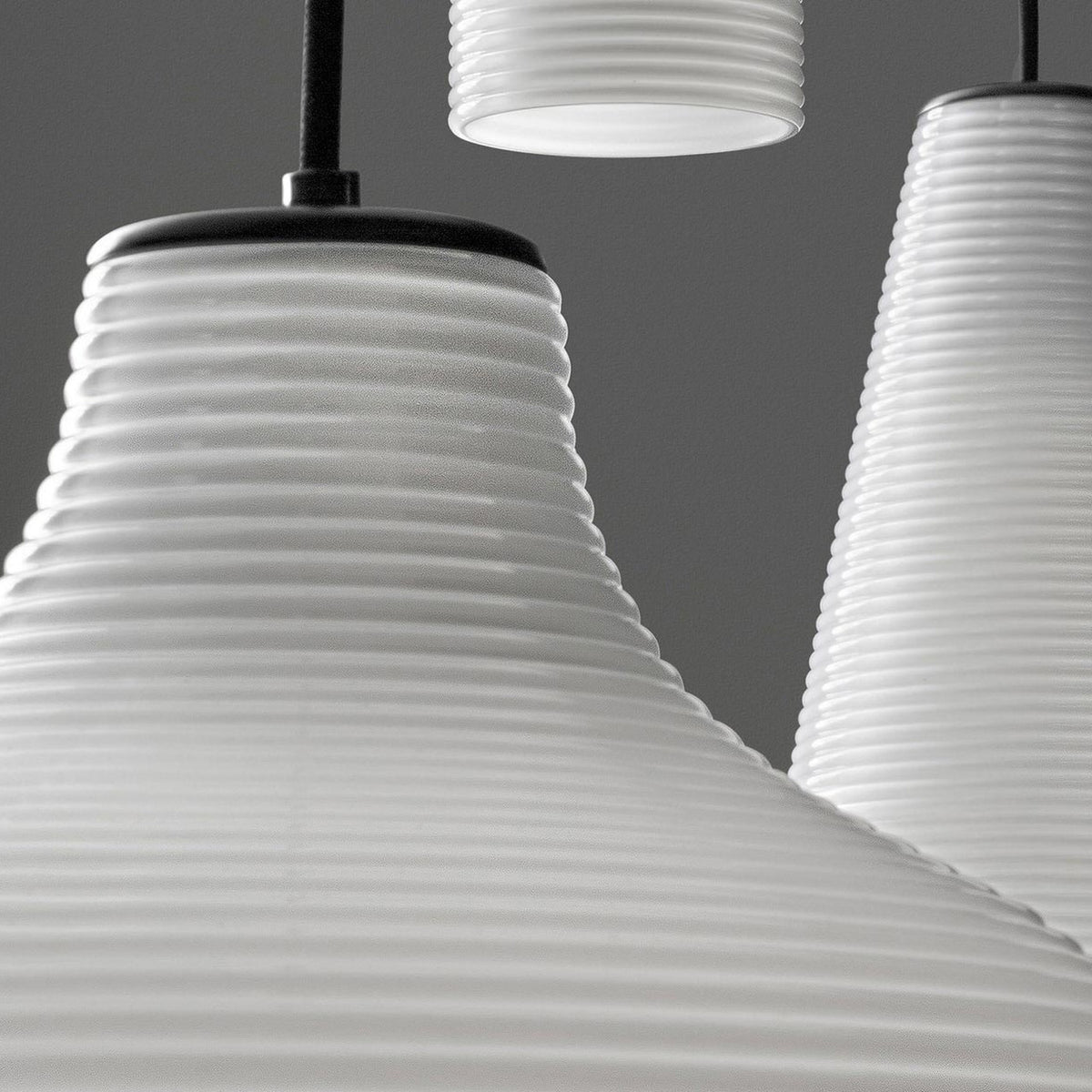 Close-up of Emma Glass LED Pendant Lights with ribbed white glass shades flaring from narrow black neck fittings, shown in a cluster against a grey background.