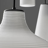 Close-up of Emma Glass LED Pendant Lights with ribbed white glass shades flaring from narrow black neck fittings, shown in a cluster against a grey background.