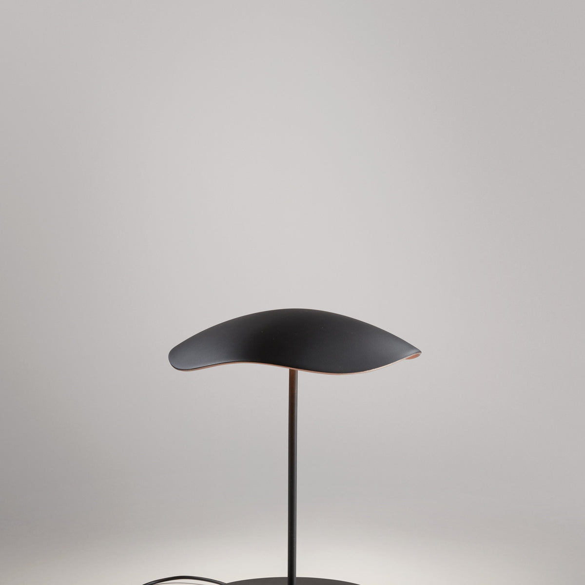 Valentina M/29 table lamp with a wavy leaf-shaped shade, black on top and copper underneath, on a slim black stem and round disc base, shown against a plain light grey background.