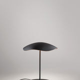 Valentina M/29 table lamp with a wavy leaf-shaped shade, black on top and copper underneath, on a slim black stem and round disc base, shown against a plain light grey background.
