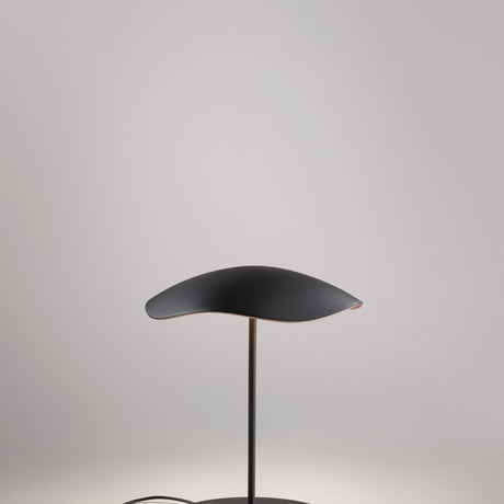 Valentina M/29 table lamp with a wavy leaf-shaped shade, black on top and copper underneath, on a slim black stem and round disc base, shown against a plain light grey background.