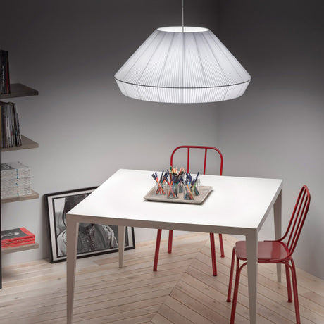 Mei 125 Ribbon Cone pendant light in white, a wide pleated cone shade above a white dining table and red metal chairs.