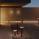 Venexia Glass LED Outdoor Floor Lamp 95cm in Corten finish, slender rust-red posts with round disc heads, illuminated in warm white light on a gravel courtyard at dusk.