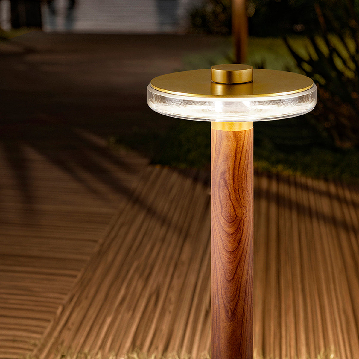 Venexia Glass LED Outdoor Floor Lamp 70cm in Wood & Matt Brass, round glass head glowing warm white atop a wood-grain column on an outdoor deck at night.