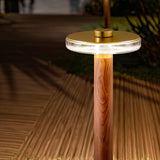 Venexia Glass LED Outdoor Floor Lamp 70cm in Wood & Matt Brass, round glass head glowing warm white atop a wood-grain column on an outdoor deck at night.