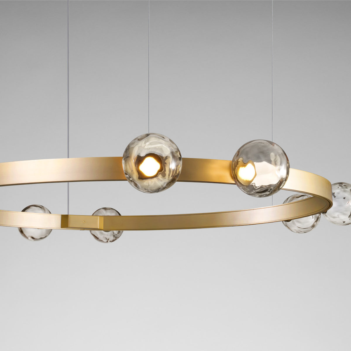 Murané R ring chandelier in Brushed Champagne finish, 110cm band with integrated LED and Smoke Grey glass spheres set above and below the ring, shown against a plain grey background.