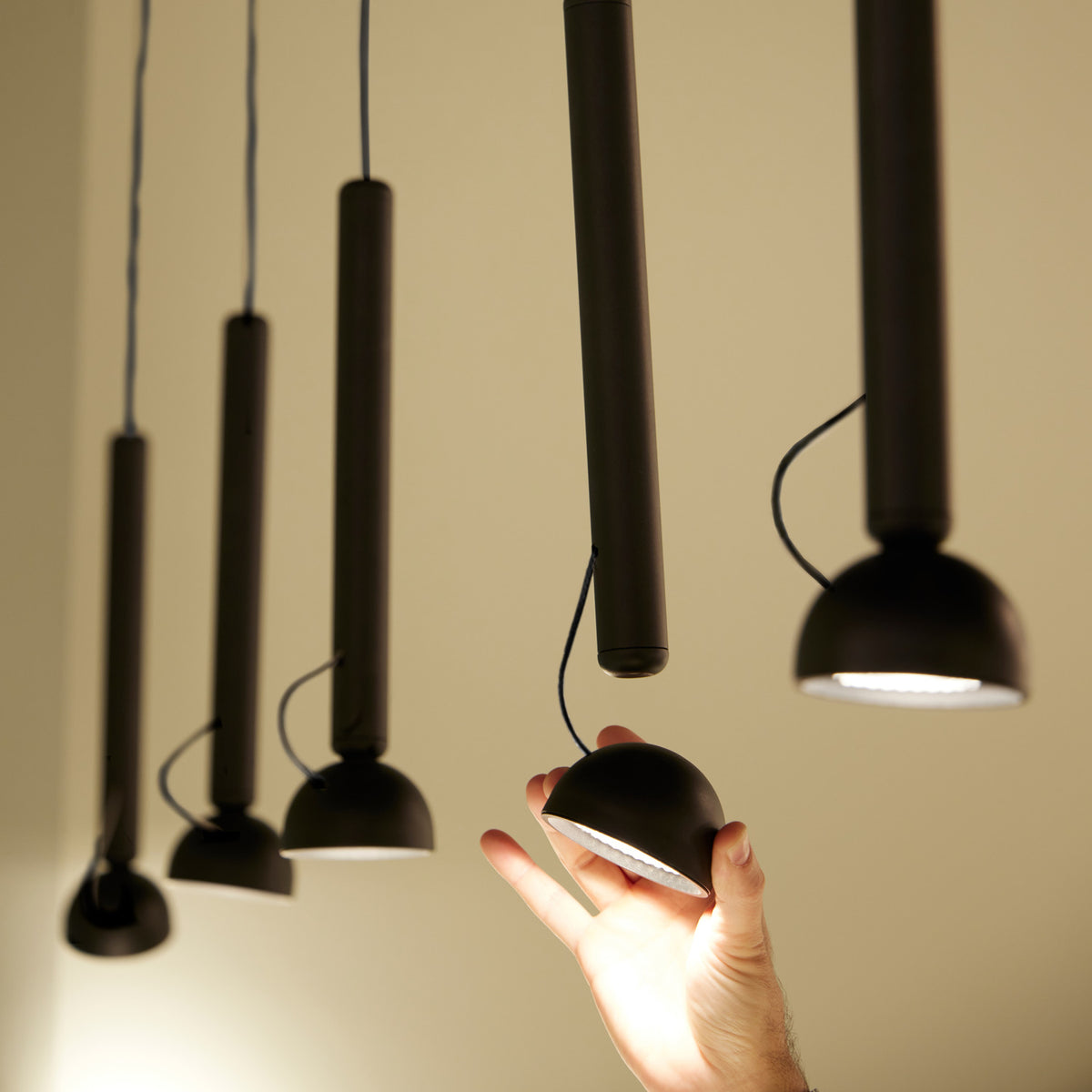 Berry S Aluminium LED Pendant Light in matte black, five slim tube pendants with small angled dome heads, one held by hand to show scale.