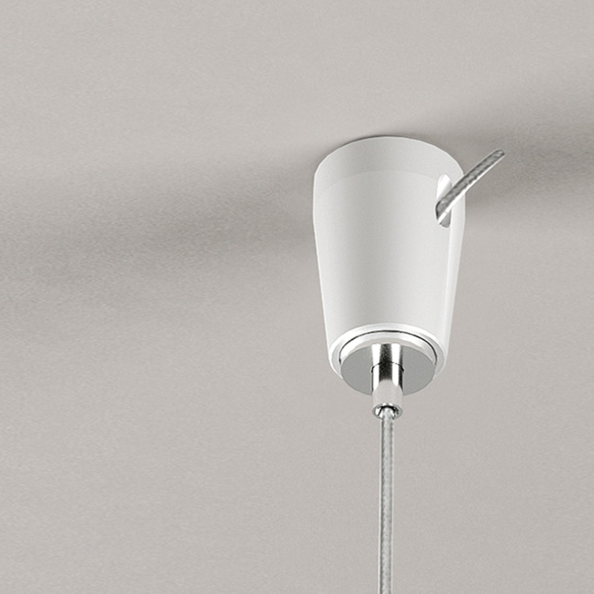Ceiling-mounted fixing for steel wire lighting, white tapered body with chrome ring and hook, suspension cable hanging below, on a plain light grey background.