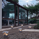 Cornet B/27 Cone LED Bollard Lights in Stone Grey with wavy tiered shades, lining a garden path beside a glass-fronted house at dusk.