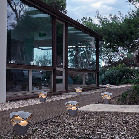 Cornet B/27 Cone LED Bollard Lights in Stone Grey with wavy tiered shades, lining a garden path beside a glass-fronted house at dusk.