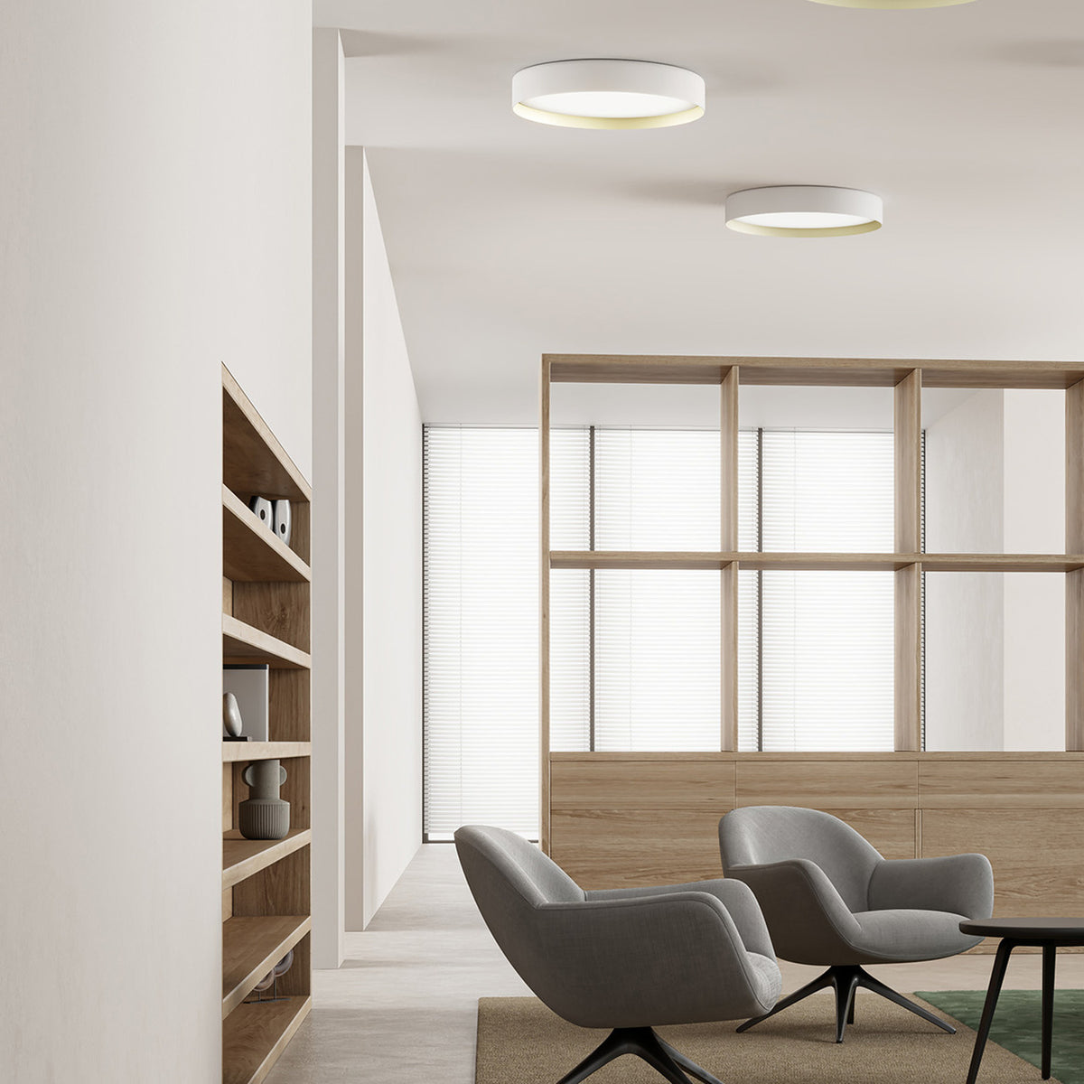 Ginevra round LED flush ceiling lights in matt white with brass inner detail, installed above a modern lounge area with wooden shelving and grey armchairs.