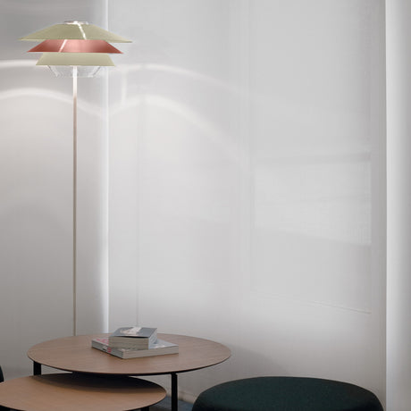 Overlay F Cognac Glass Tiered Floor Lamp with layered conical shades in yellow, grey and beige tones, slim stem and round base, shown beside a coffee table in a living room.